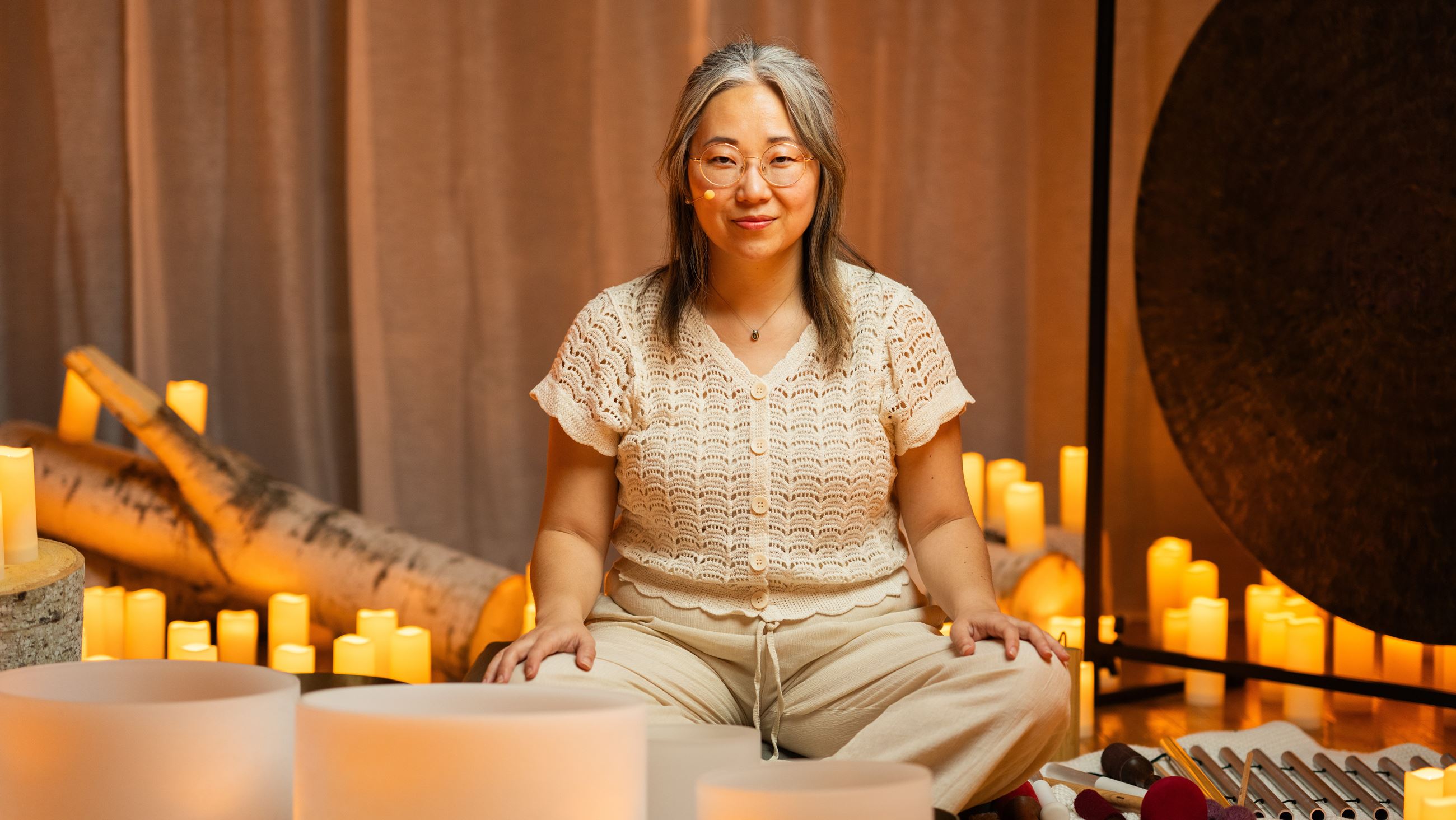 wellness practitioner sits with sound tools surrounded by candles